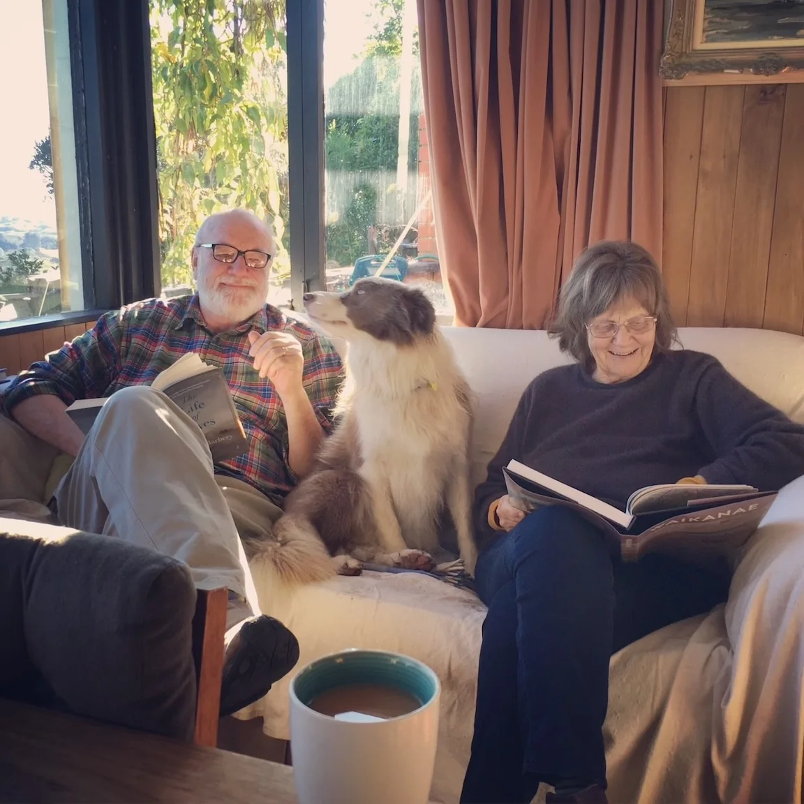 Pam reading on a sofa with a family member and dog